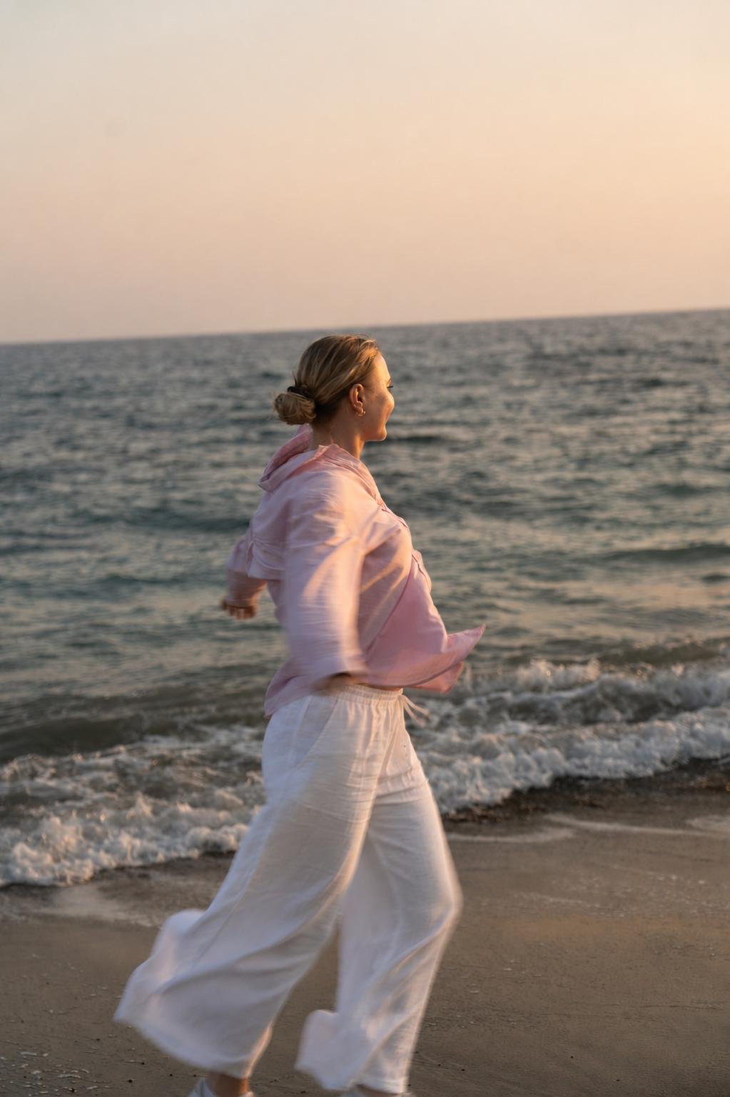 Lilli Schmid geht im Abendlicht am Strand entlang, die Arme leicht ausgebreitet, der Blick geht aufs Meer